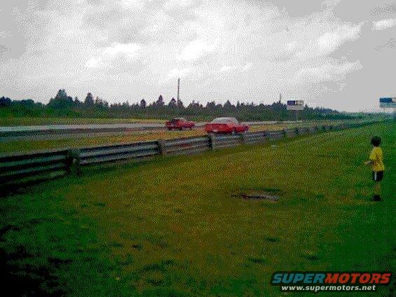 two red cars racing on a track with a kid watching from the grass