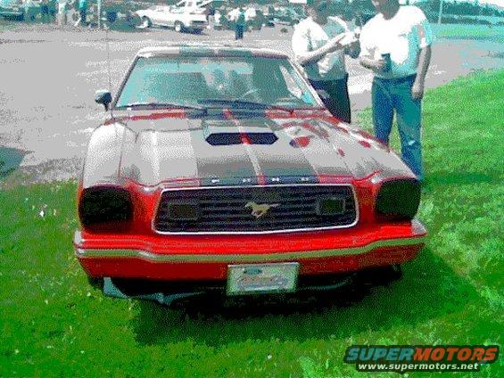 Red car with black racing stripes and a hood scoop, front view