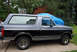 1995 Ford Bronco - A two-tone black and grey Ford Bronco SUV is parked on a concrete driveway next to a house.