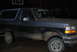 1995 Ford Bronco - A two-tone Ford Bronco is parked outside at night, covered in dirt. A person is visible in the driver's seat.