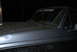 1995 Ford Bronco - The front corner of a muddy 1995 Ford Bronco is visible, with "DELUXE" lettering on the windshield.