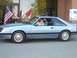 1986 Ford Mustang - Side view of a light blue 1986 Ford Mustang coupe parked outside a building with American flags.