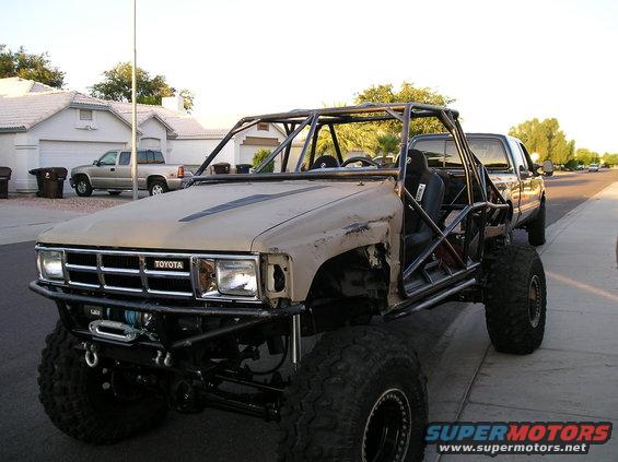 Customized Toyota truck with a roll cage and large tires, parked on a street