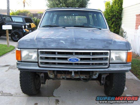 Gray Ford Bronco front view, faded paint, aftermarket bumper, parked in driveway with Jeep behind