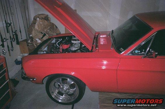 Red 1967 Ford Mustang, hood open showing engine. Chrome wheels visible