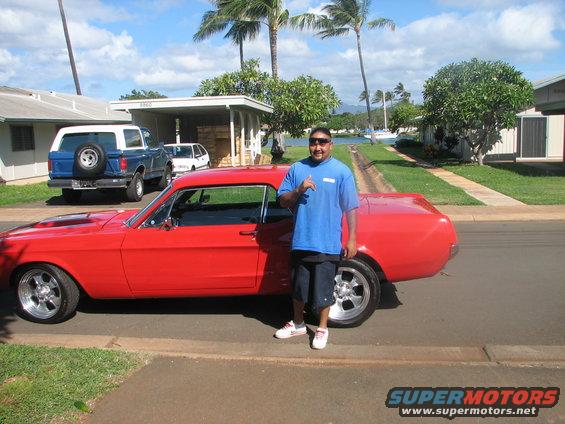 Red 1967 Ford Mustang coupe with aftermarket wheels, parked on a residential street