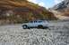 1990 Chevrolet Suburban - A 1990 Chevrolet Suburban navigates a rocky, dry riverbed during autumn, with colorful foliage on the surrounding hills.