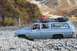 1990 Chevrolet Suburban - An SUV navigates a challenging rocky path, its tires deep in the gravel, with autumn foliage on the surrounding hills.