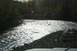 1990 Chevrolet Suburban - A river flows over rocks with trees on the bank under a bright sun.