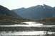 1990 Chevrolet Suburban - A wide, rocky riverbed with shallow water reflecting the sunlight, set against a backdrop of mountains.