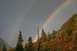 1990 Chevrolet Suburban - A double rainbow appears in the sky above a wooded hillside with trees showing fall colors.