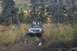 1990 Chevrolet Suburban - A person stands in tall grass next to an off-road vehicle navigating a muddy trail.