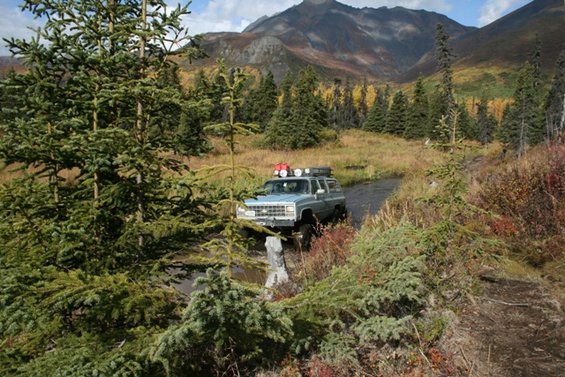 Light blue 1990 Chevrolet Suburban driving through water with roof rack and extra lights