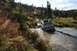 1990 Chevrolet Suburban - A gray van navigates a muddy stream in a wooded, autumnal landscape.