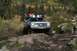 1990 Chevrolet Suburban - A silver SUV navigates a challenging off-road trail with a rocky and muddy terrain.