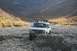 1990 Chevrolet Suburban - This light blue SUV navigates a challenging rocky terrain, equipped with a roof rack carrying extra fuel and a spare tire.