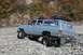 1990 Chevrolet Suburban - A light blue SUV navigates a rocky terrain with a person in the driver's seat and another passenger visible.