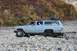1990 Chevrolet Suburban - A light blue Chevrolet Suburban navigates a rocky terrain with fall foliage in the background.