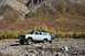 1990 Chevrolet Suburban - A light blue 1990 Chevrolet Suburban is parked on a rocky, off-road path with mountains and autumn foliage in the background.