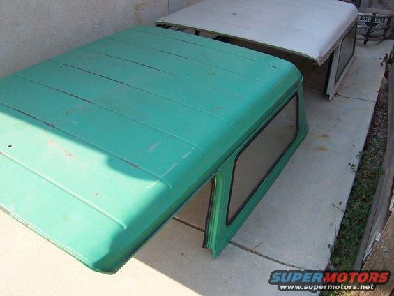 Two vehicle hardtops, one green and one white, sit on a concrete surface