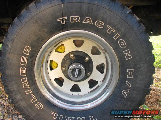 Close-up of a "Trail Climber Traction H/T" tire on a white-spoked wheel with yellow brake calipers visible