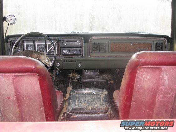 Interior of a 1978 Ford Bronco with red seats, green dashboard, and aftermarket gauge