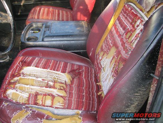 worn red and striped fabric seats with torn upholstery, center console with cup holders, and part of a steering wheel