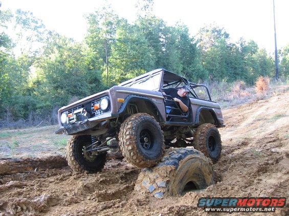 Brown Ford Bronco with large tires navigating a muddy hill, one tire stuck under a rock