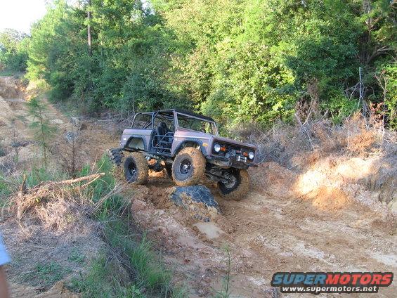 Modified Ford Bronco with roll cage and large tires navigating a muddy incline