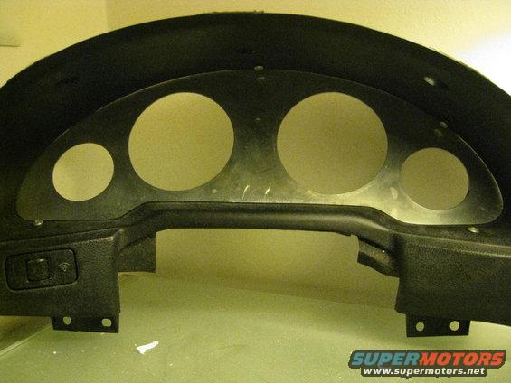 Car dashboard instrument cluster housing with circular cutouts for gauges. Includes a switch panel on the left