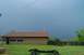 1980 Ford Bronco - A vehicle frame sits on a grassy lawn with a house and a dark, stormy sky in the background.