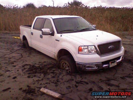 White Ford F-150 stuck in mud, front 3/4 view, mid-2000s model