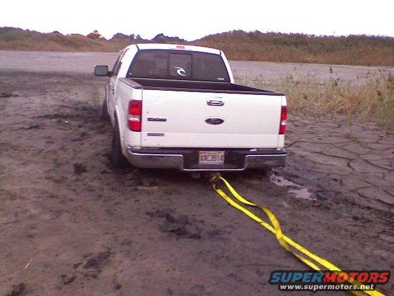 White Ford F-150 stuck in mud, rear view, yellow tow strap attached