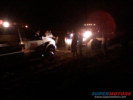 People gathered around vehicles at night, with headlights on