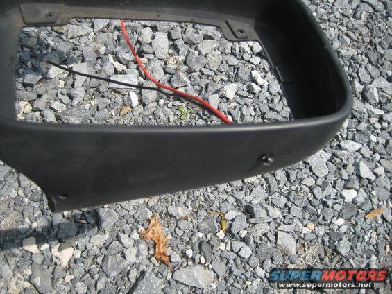 Black automotive part with red and black wires, lying on gravel