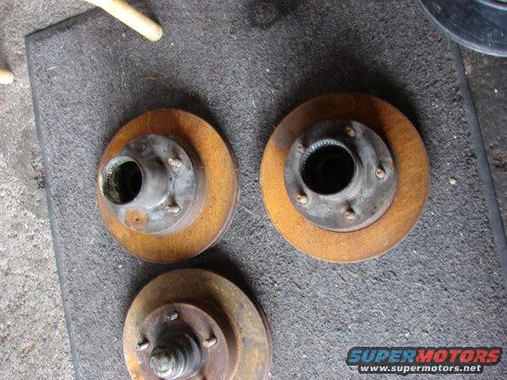 Three rusty brake rotors with hubs on a gray mat