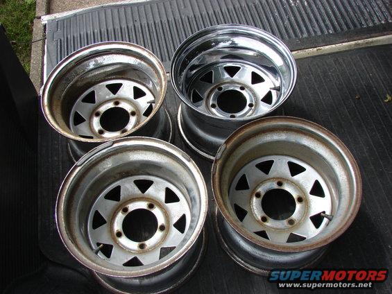 Four steel wheels with triangular cutouts, some showing rust, resting on a truck bed