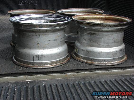 Four used aluminum rims with rust on the inner barrels, resting in a truck bed