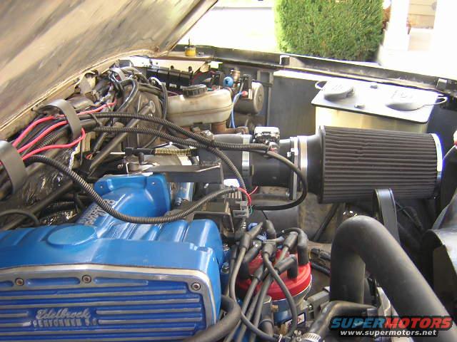 Engine bay with blue Edelbrock Performer 5.0 valve covers and a black cone air filter. Some wiring and hoses are visible