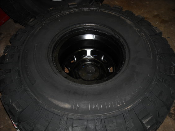 Close-up of a large off-road tire with a black rim inside. Some chalk marks are visible on the tire sidewall