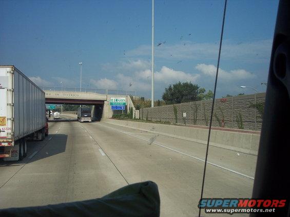 Highway overpass with "Welcome to Illinois" sign and trucks on the road