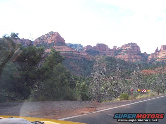 Yellow car dashboard and windshield view of red rock mountains and a road with a striped barrier