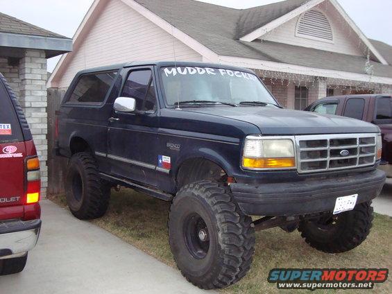 Lifted 1995 Ford Bronco with large off-road tires parked next to a red SUV