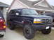 1995 Ford Bronco - This lifted Ford Bronco is parked in a driveway next to another SUV, ready for off-road adventures.