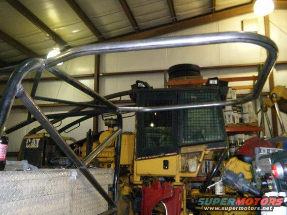 Yellow construction vehicle with roll cage, tire on top, in a workshop