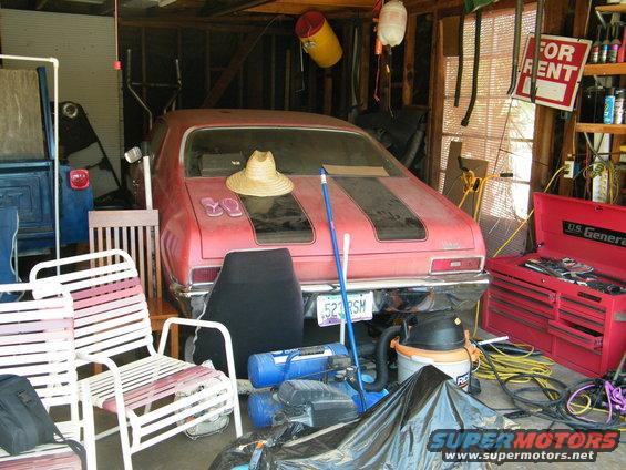 Red coupe with black stripes on the hood and trunk, parked in a cluttered garage. License plate reads 523 RSM