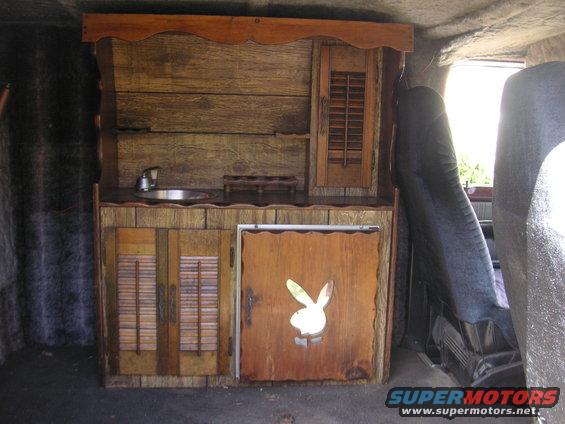 Interior of a van with a wooden kitchenette, sink, and a door with a Playboy bunny cutout