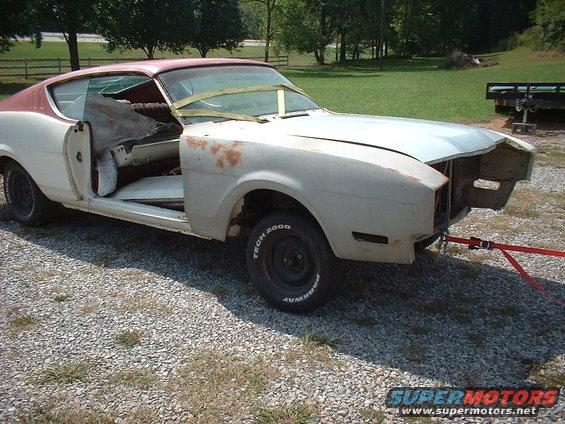 Project car, possibly a 1969 Mercury Cyclone, with doors removed and interior exposed, sitting on gravel