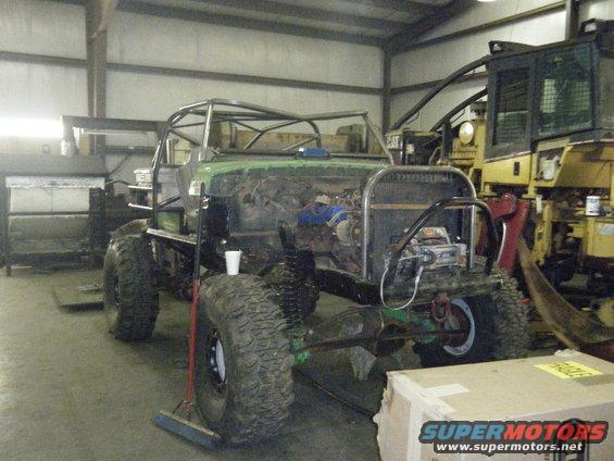 custom off-road vehicle build with roll cage, large tires, and exposed engine, parked next to heavy machinery
