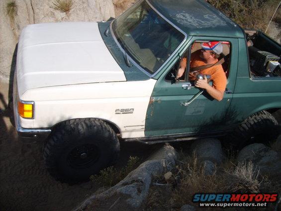 Ford F-250 off-roading over rocks, driver in orange shirt and hat